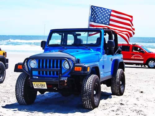Blue Jeep Wrangler on the beach flying a large American flag
