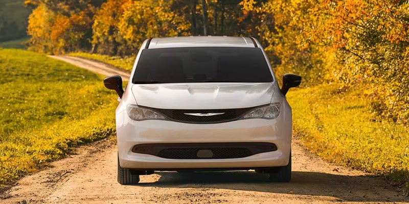 A white minivan is centered on a narrow dirt or gravel road