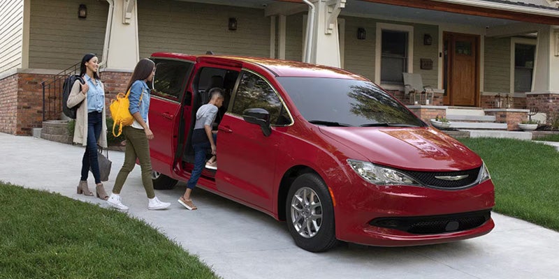 A red minivan is parked in a residential driveway in front of a house