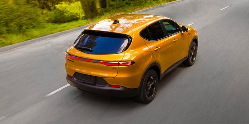 A gold/orange crossover SUV is driving on a paved road surrounded by greenery
