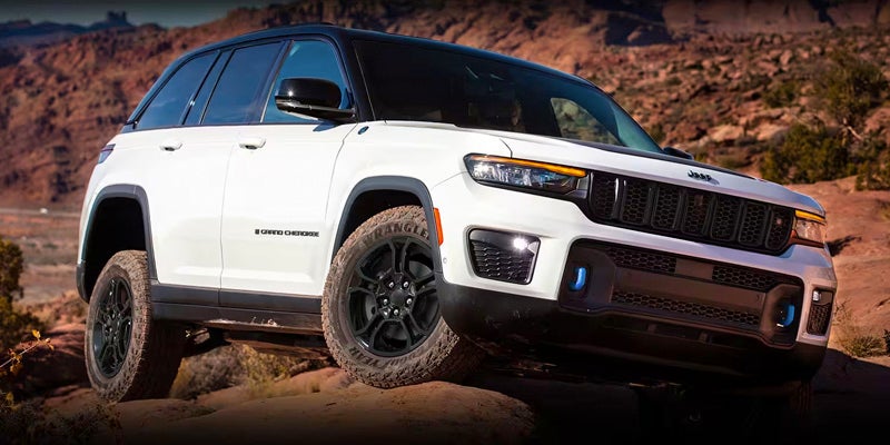 A white 2023 Jeep Grand Cherokee Trailhawk 4xe on a rocky off-road trail in a desert landscape.