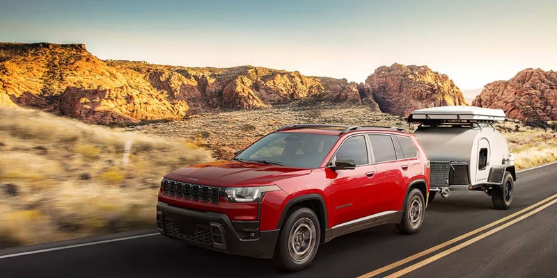 Red Jeep SUV towing a camper trailer on a scenic desert highway
