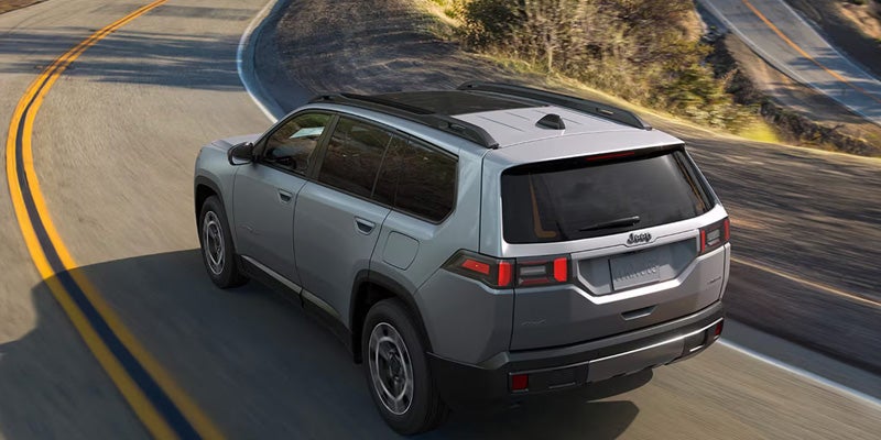 Gray Jeep SUV driving on a winding road with mountain scenery