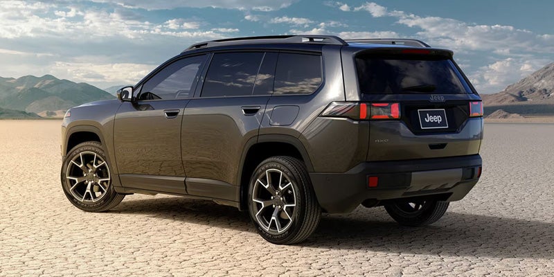 A dark gray SUV is parked on a dry, cracked desert landscape