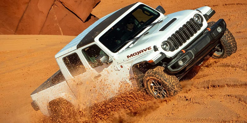 White Jeep Wrangler driving through sand dunes with mud and sand spray