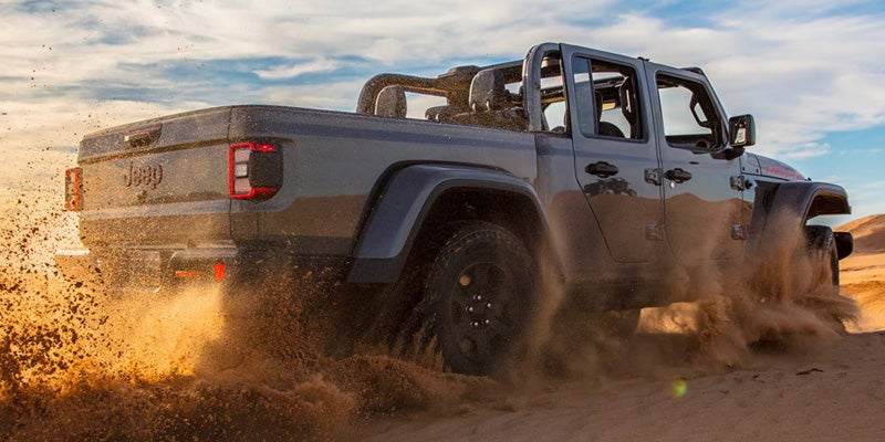 Gray Jeep Gladiator pickup truck driving off-road through dirt terrain