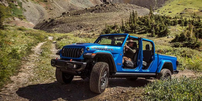 Blue Jeep Wrangler with removable doors driving on a mountain trail
