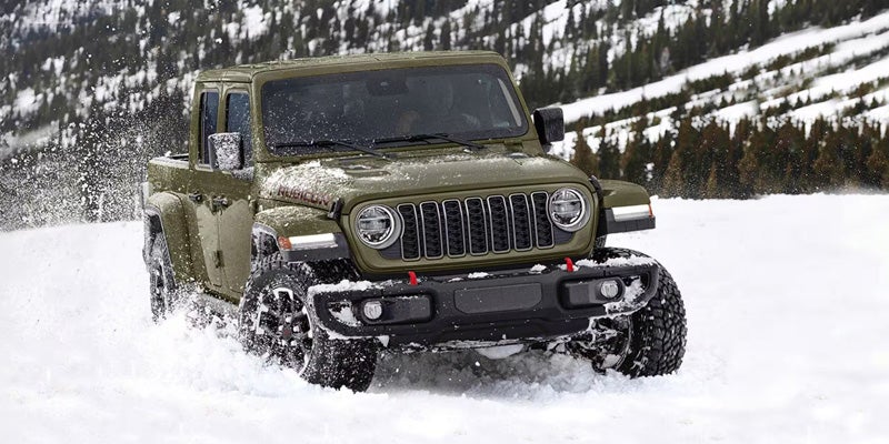 Green Jeep Wrangler driving through deep snow in a winter landscape