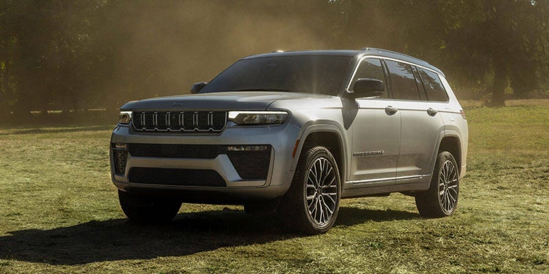 Gray Jeep Grand Cherokee SUV driving on a grassy trail in an outdoor setting