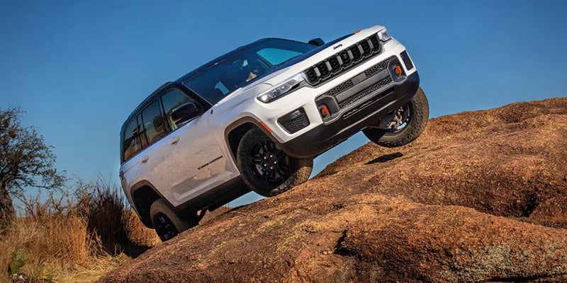 A white SUV is driving or positioned on a rocky incline in an off-road environment