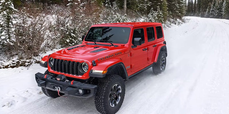 Red Jeep Wrangler driving on a snowy road in a winter landscape
