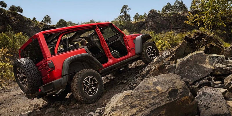 Red Jeep Wrangler navigating a rocky mountain trail with open doors