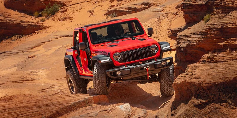 Red Jeep Wrangler driving through sandy desert terrain off-road