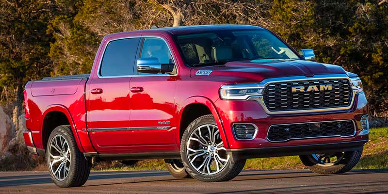 A new shiny red Ram pickup truck with chrome accents, side view mirrors and wheels, parked on asphalt