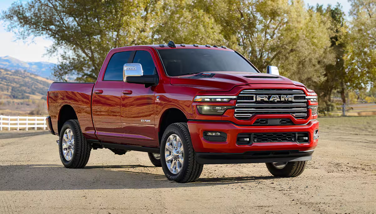 A shiny red Ram 3500 pickup truck parked on a dirt road, with trees and mountains in the background