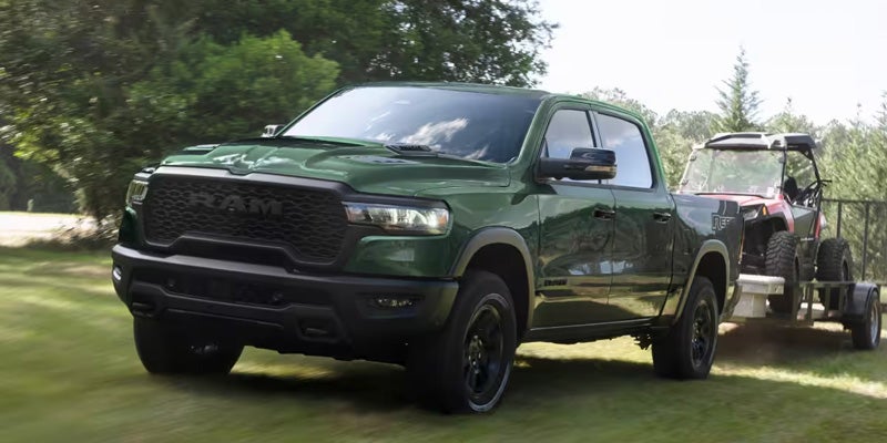 Green Ram pickup truck towing a trailer on a tree-lined road