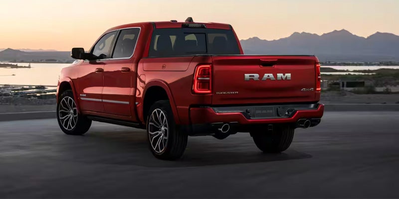 Rear view of a red Ram pickup truck with dual exhaust, parked on asphalt at sunset near mountains and water